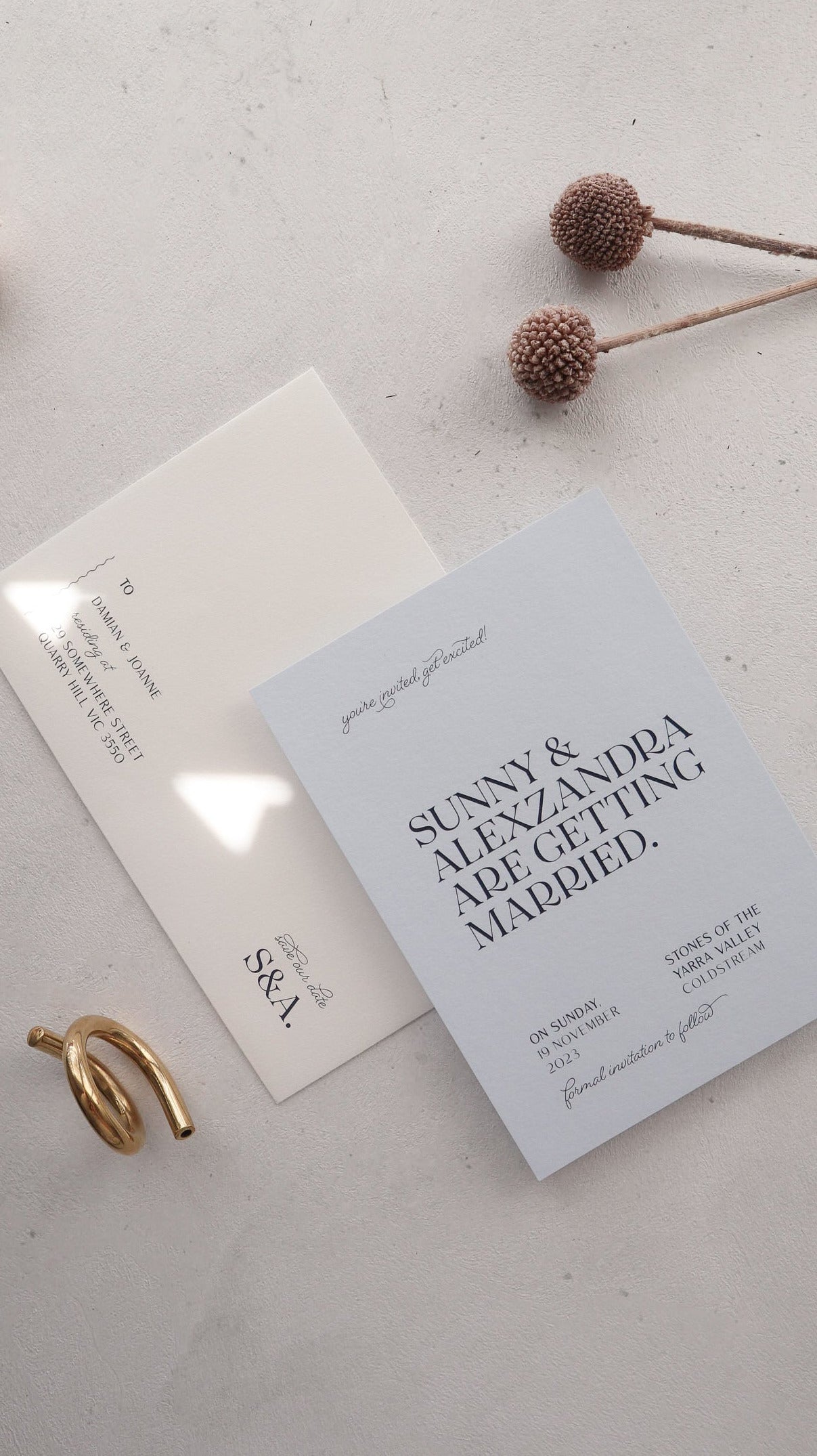 Wedding invitation card on a light surface with a gold ring and dried flowers.